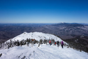 hikers traverse snowy summit with blue sky in background