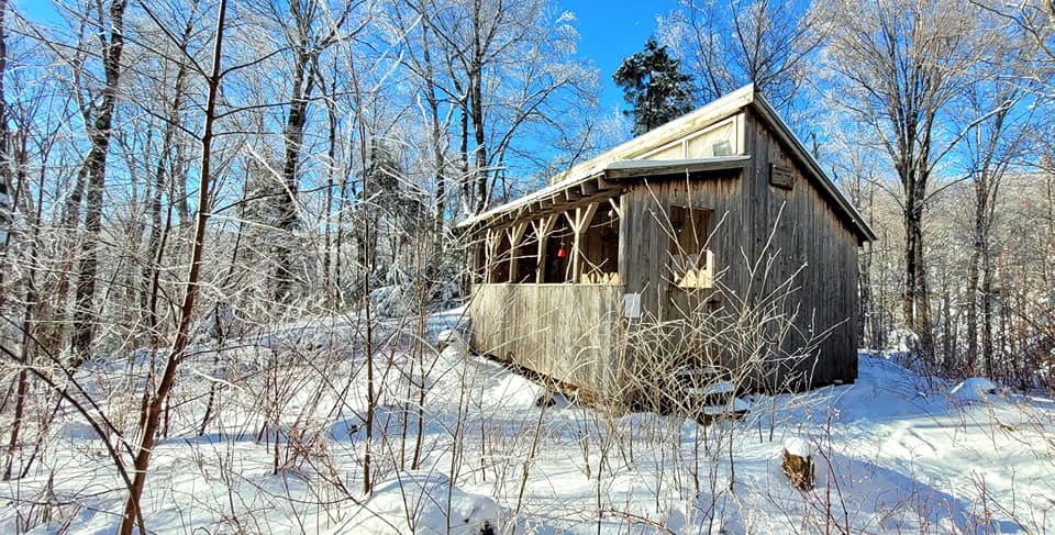 A wooden, four-walled cabin in snow provides shelter from winter hiking