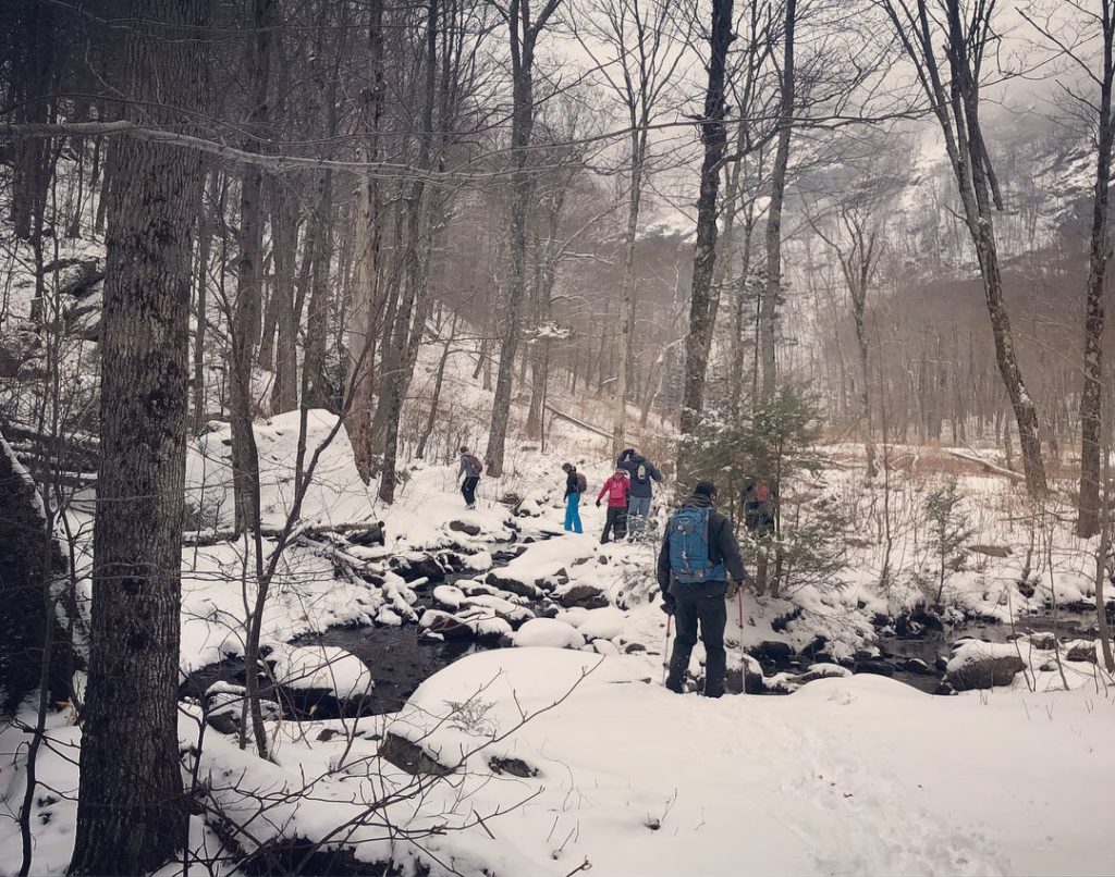 Hikers cross a river in a snowy terrain on this moderate winter hike.