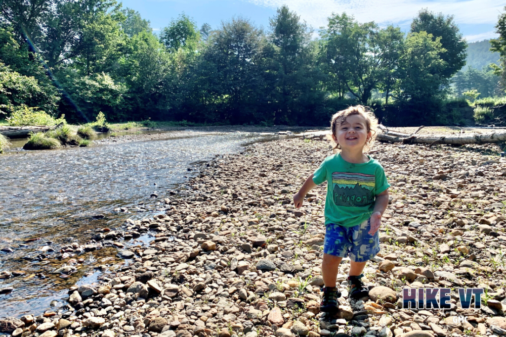 Quinn on rocky shore along river at Stowe Recreation Path, a recommendation in our mud season trail index