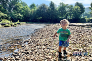Quinn on rocky shore along river at Stowe Recreation Path