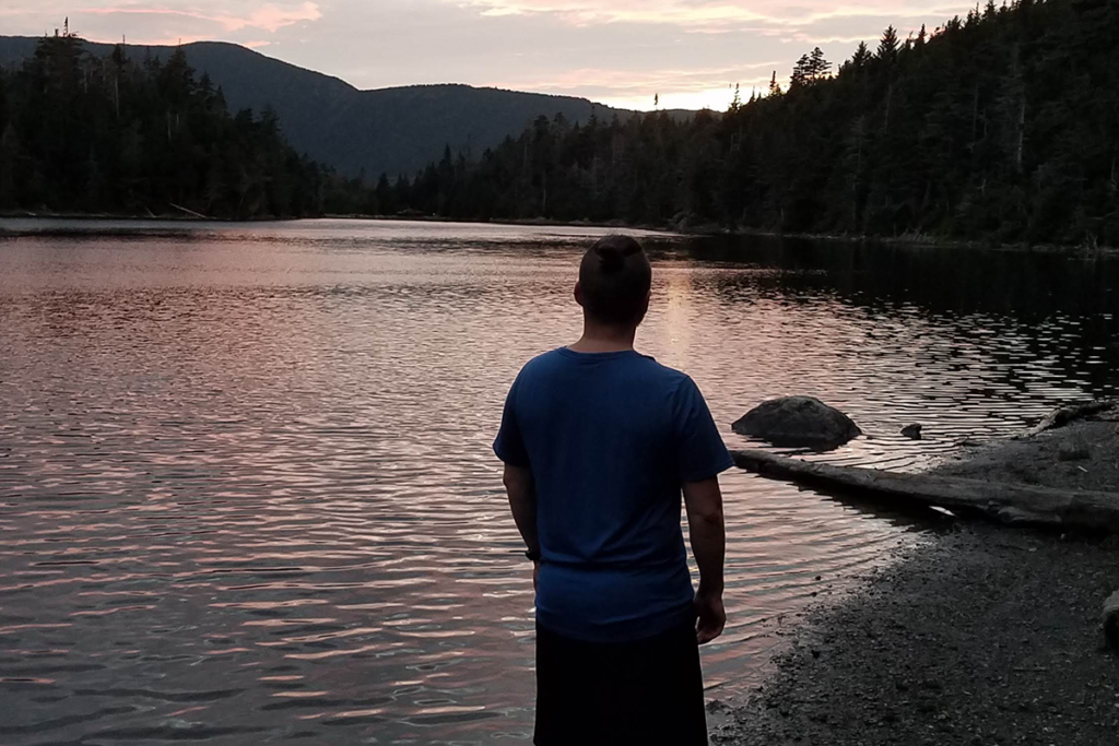 Aubri Drake, a transgender thru-hiker, overlooks a lake as the sun goes down.