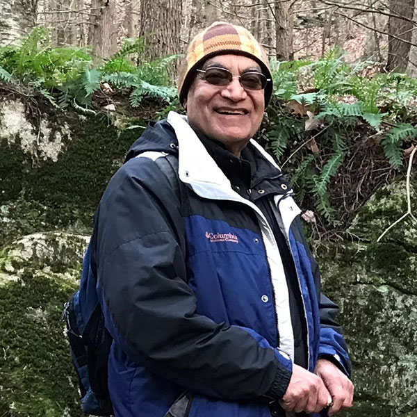 Ram Moennsad stands layered in front of mossy, lichen covered boulder