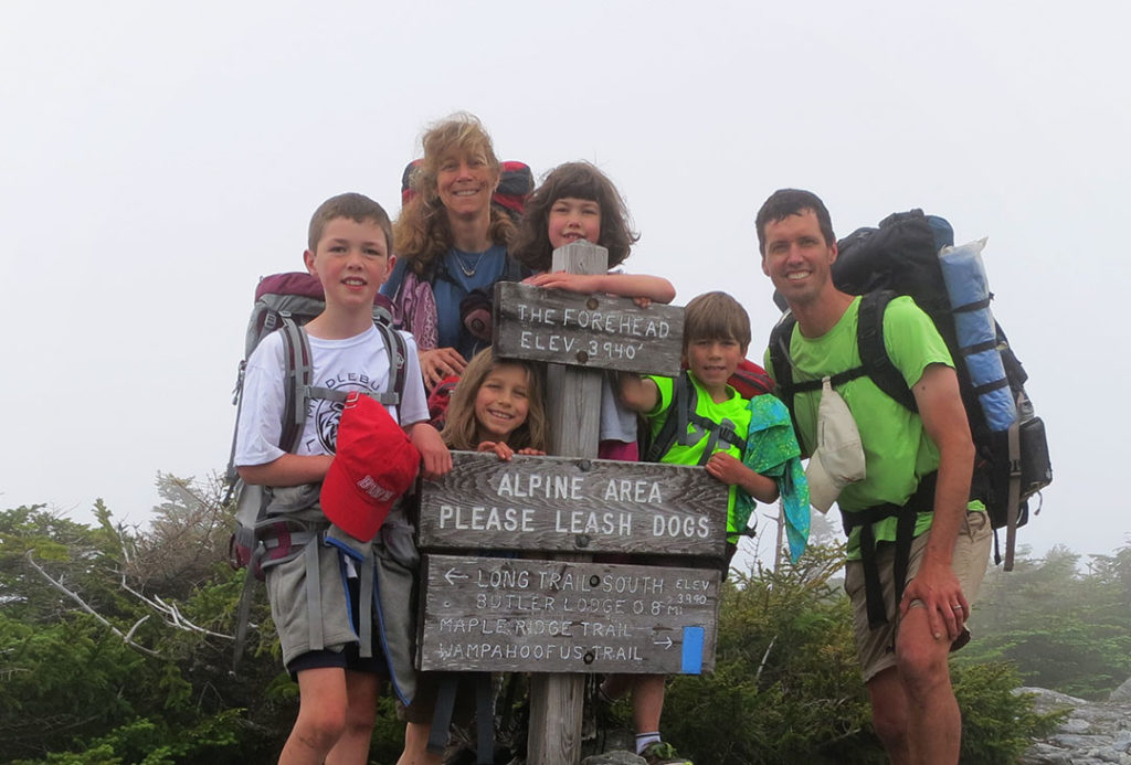 End-to-End family poses by signage in alpine zone.