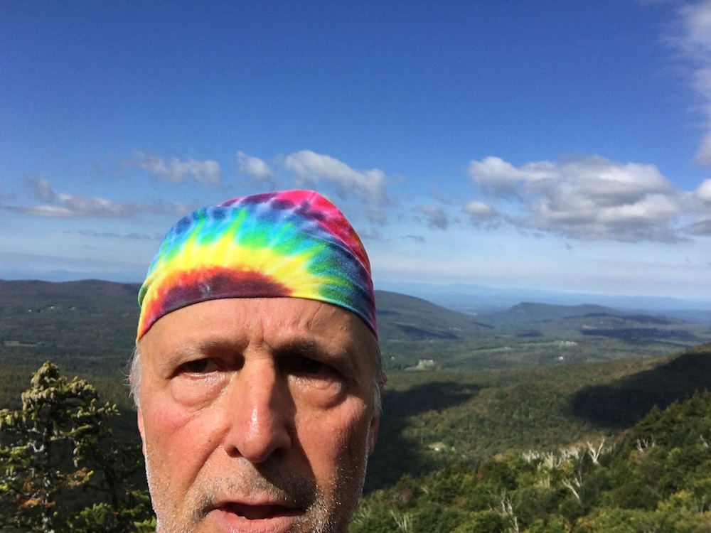 Selfie of hiker in rainbow tie dye bandana on a summit