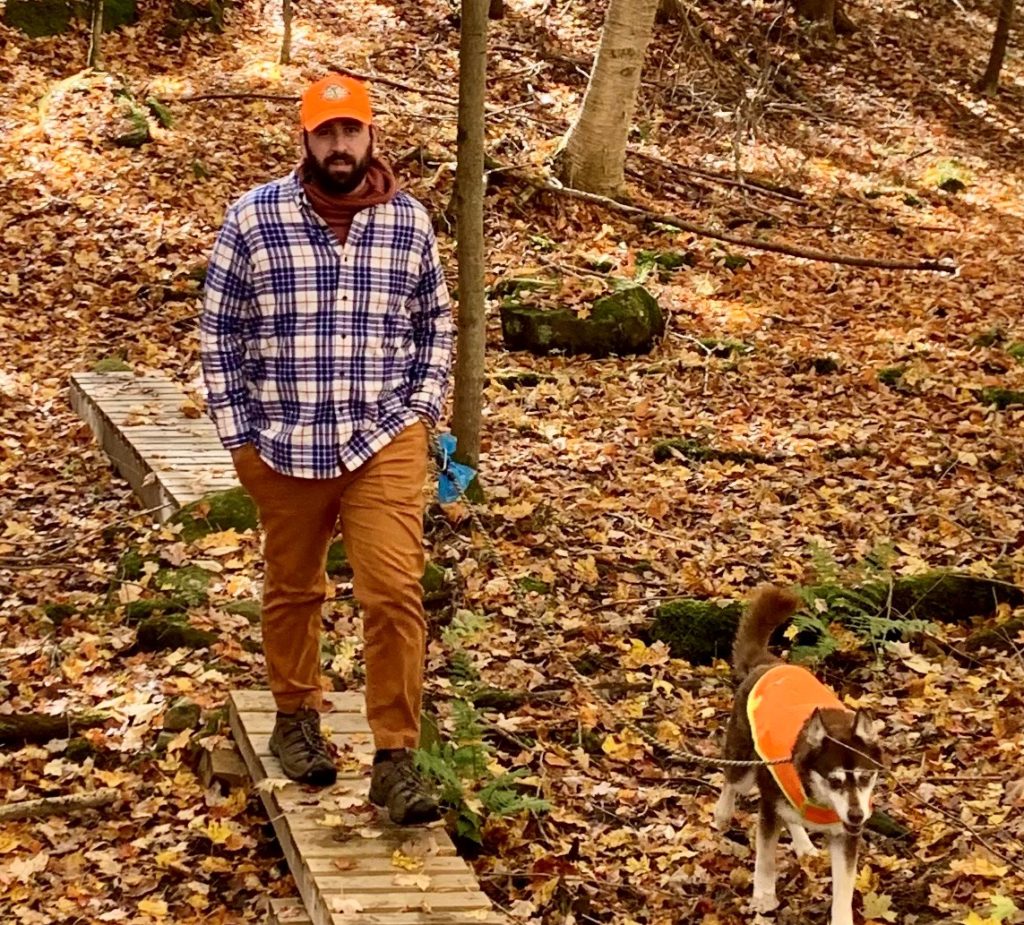 hiker and dog wearing blaze orange amidst fall leaves