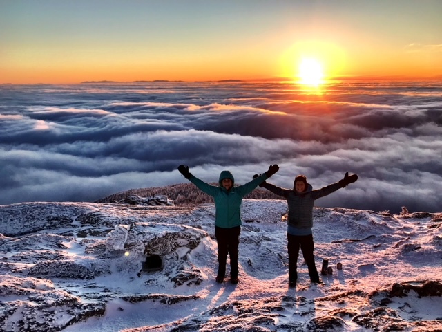 Two hikers pose for a photo at sunrise from Camels Hump.