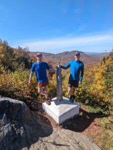 two men in blue shirts pose on either side of the journey's end monument