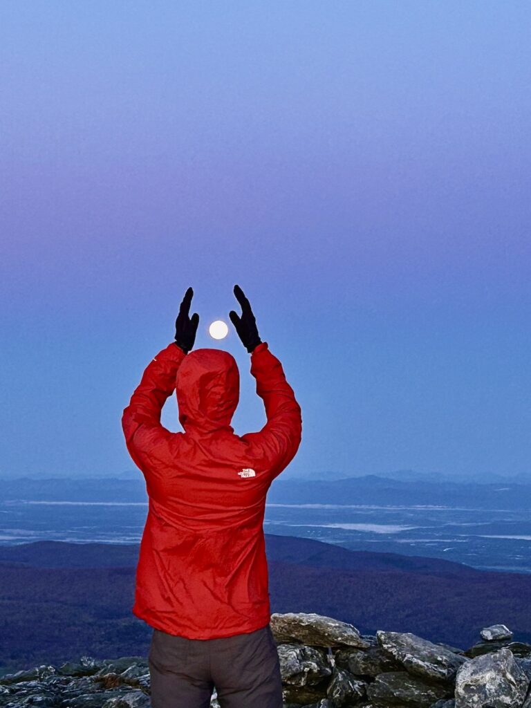 a hikers frames the moon in his hands