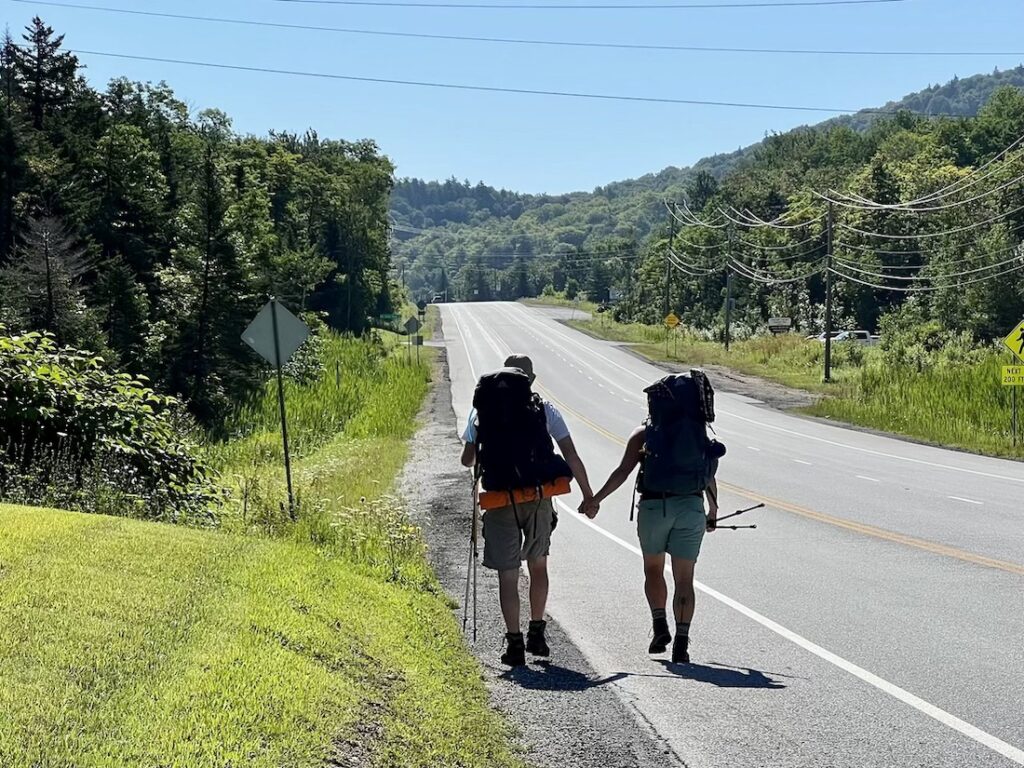 two hikers walk hand in hand down a paved road
