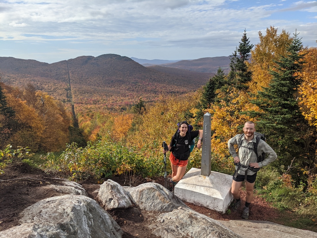 two people with journey's end monument with view of fall foliage and Canadian border in the background