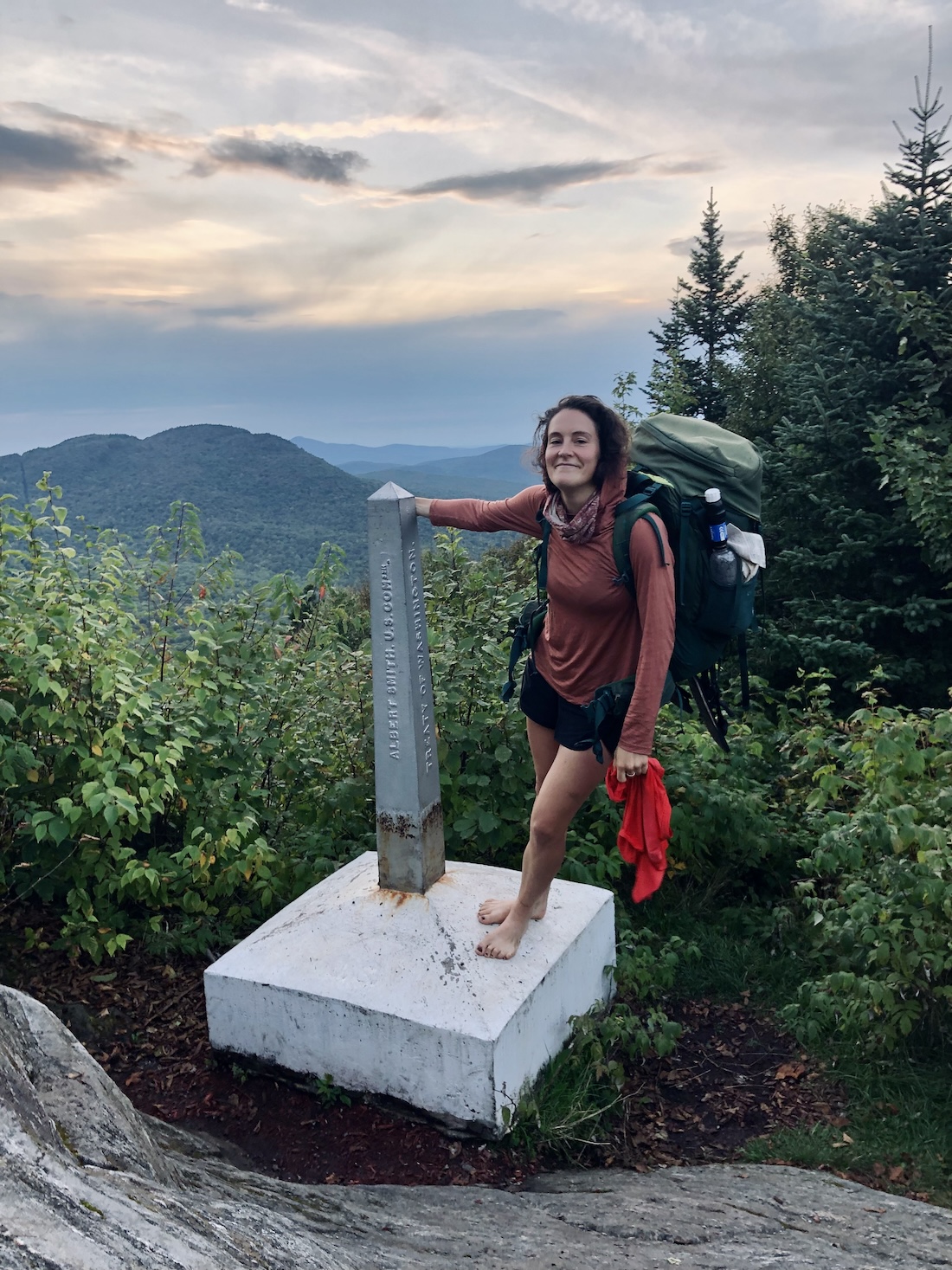 barefoot woman with backpacking backpack leans on journey's end monument