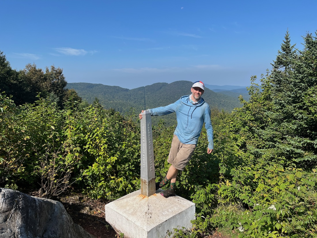 man in blue hoodies and white hat leans on the journey's end monument
