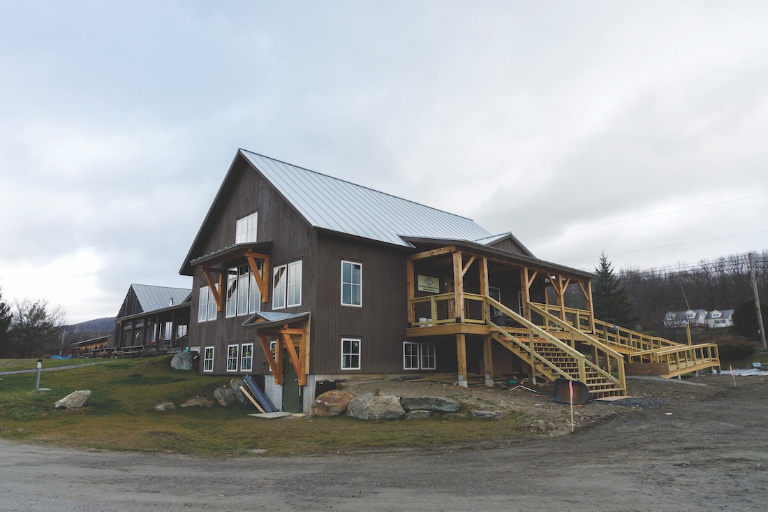 exterior shot of a timber-frame building, painted dark brown with a green roof, windows, large porch and accessibility ramp
