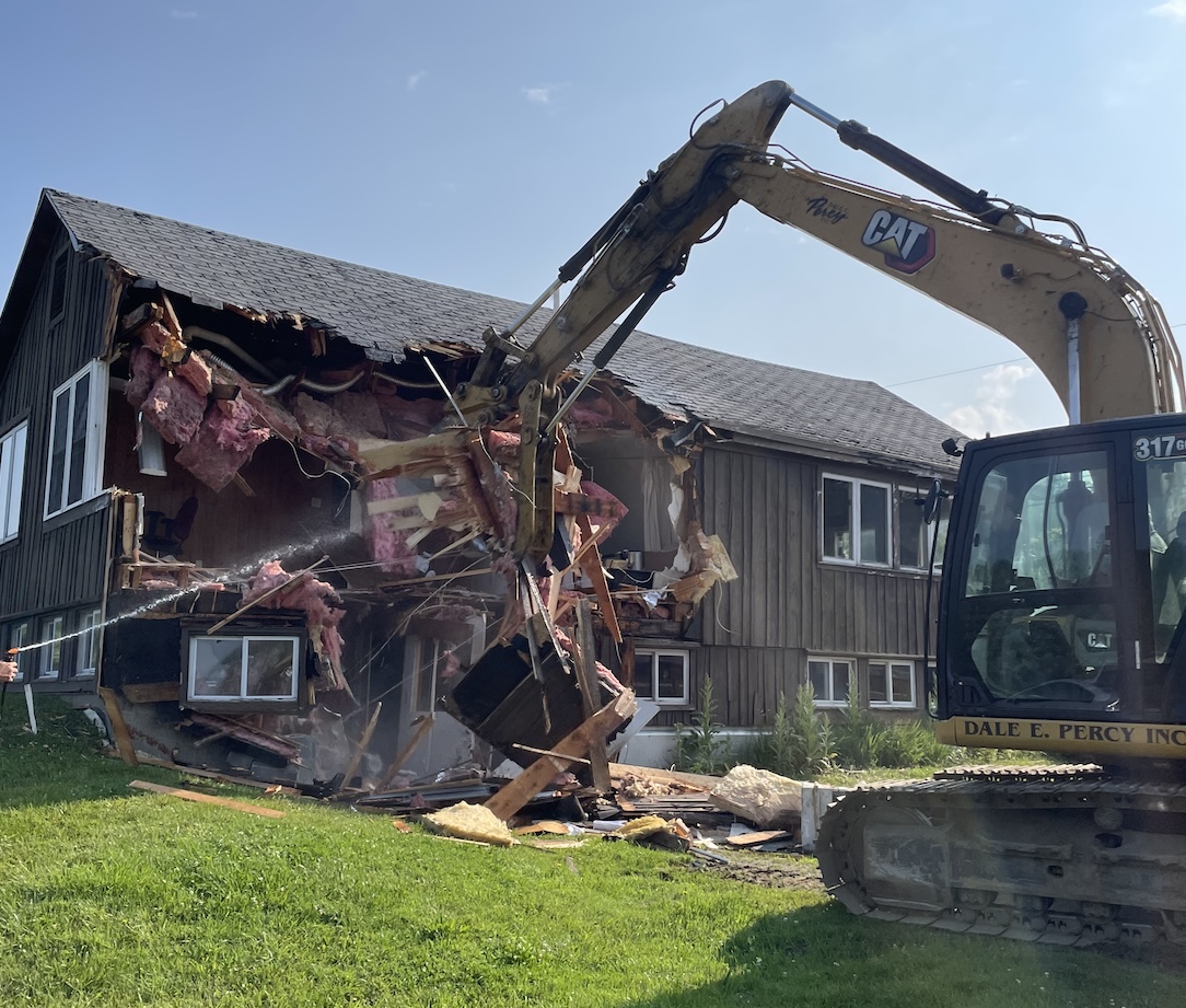 a large backhoe destroys a brown building