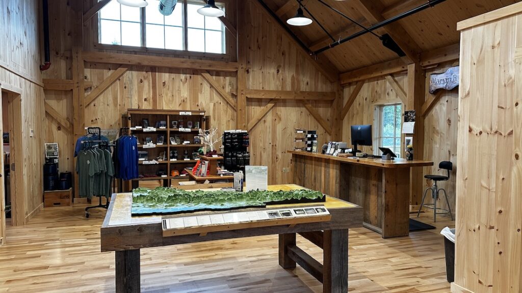 a bright wood paneled room with a large topographical relief map, displays of clothing and books, and a big desk with a computer on it