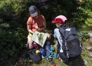 two hikers look at a map with hiking gear around them